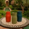 Ensemble de 3 vases en céramique tadelakt H 20 à 23 cm Ensemble de 3 vases de couleurs différentes, en céramique tadelakt, présentés sur une table en zellige dans un jardin - Kanel Déco